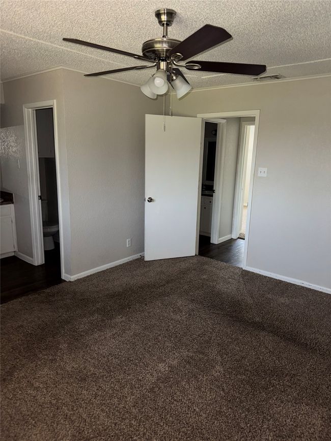 Unfurnished bedroom with dark colored carpet, a textured ceiling, connected bathroom, baseboards, and ceiling fan | Image 13