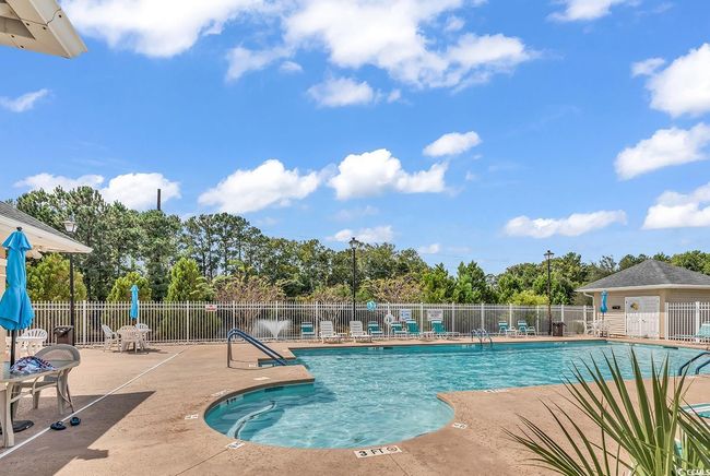 Community pool with a patio area and view of scattered trees | Image 35