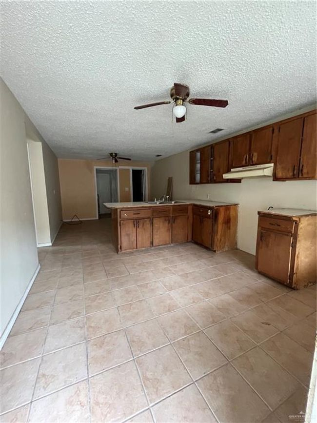 Kitchen with ceiling fan, range hood, light tile patterned flooring, a peninsula, and a textured ceiling | Image 8