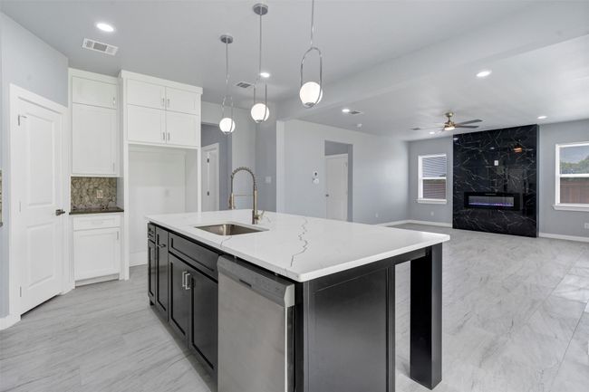 Kitchen with stainless steel dishwasher, a ceiling fan, light stone counters, white cabinets, and pendant lighting | Image 16