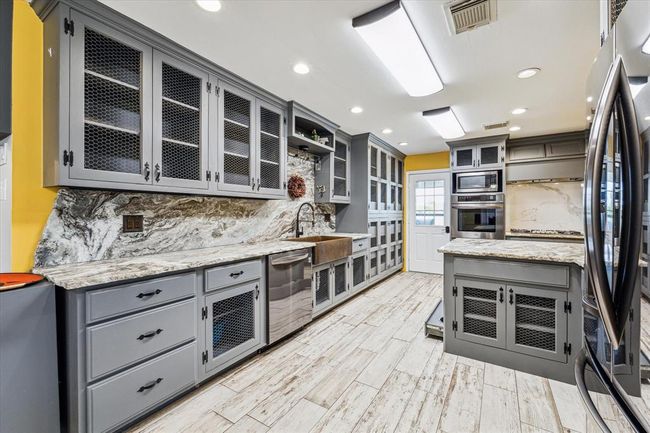 What a standout kitchen! This fully custom updated kitchen is a dream, featuring sophisticated all black stainless appliances, open shelving cabinetry with and option to place glass or solid fronts. direct access to the back patio for ease and convenience of outdoor entertaining. There is even a pull-out pet feeding station | Image 16