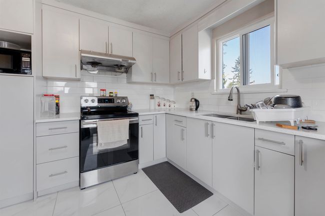 Kitchen with electric stove, under cabinet range hood, light countertops, tasteful backsplash, and black microwave | Image 9