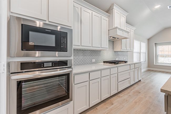 Kitchen with appliances with stainless steel finishes, lofted ceiling, backsplash, light wood-style flooring, and white cabinets | Image 16