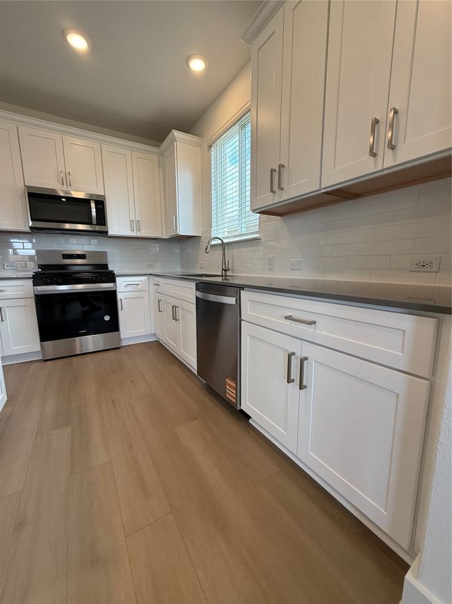 Kitchen featuring stainless steel dishwasher, stove, tasteful backsplash, wood finished floors, and a sink | Image 20