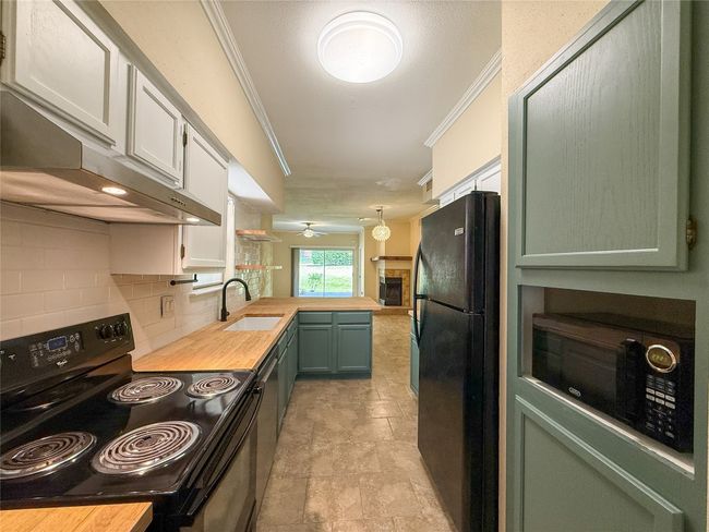 Kitchen with black appliances, green cabinetry, decorative backsplash, crown molding, and a peninsula | Image 15