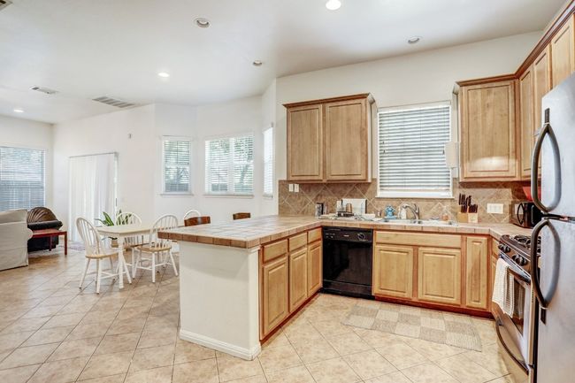 Kitchen featuring black dishwasher, stainless steel gas stove, a peninsula, tile countertops, and light tile patterned flooring | Image 6