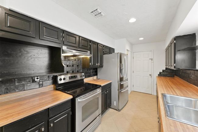 This kitchen features sleek black cabinets, stainless steel appliances, and warm wood countertops, creating a modern and functional space. | Image 15