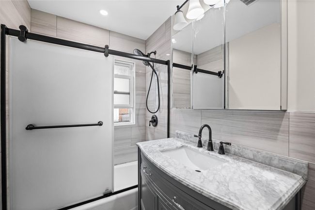 Full bathroom featuring tile walls, bath / shower combo with glass door, vanity, decorative backsplash, and recessed lighting | Image 28