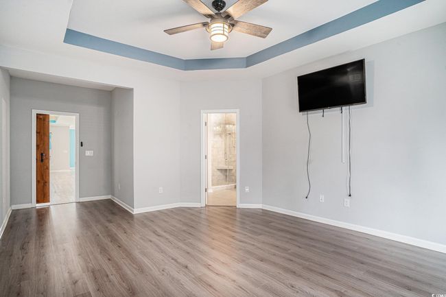 Unfurnished living room featuring ceiling fan, wood finished floors, and a raised ceiling | Image 16