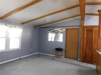 Empty room with light carpet and vaulted ceiling with beams | Image 3