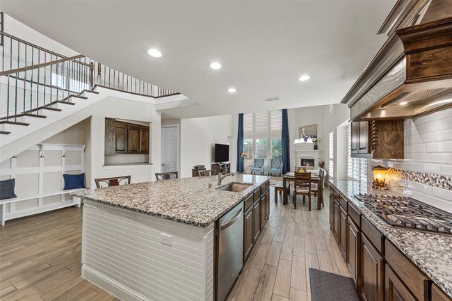 Kitchen with stainless steel appliances, open floor plan, a sink, light wood finished floors, and a fireplace | Image 12