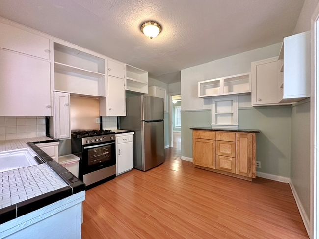 Kitchen with open shelves, stainless steel appliances, decorative backsplash, light wood-style flooring, and a textured ceiling | Image 20