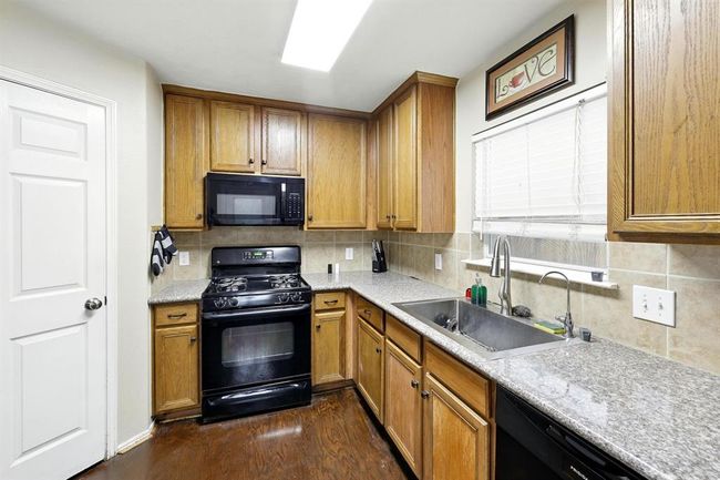 Well-equipped kitchen featuring granite-look countertops, tile backsplash, gas range, built-in microwave, and ample cabinet storage. A central sink under the window offers natural light and functionality. | Image 7