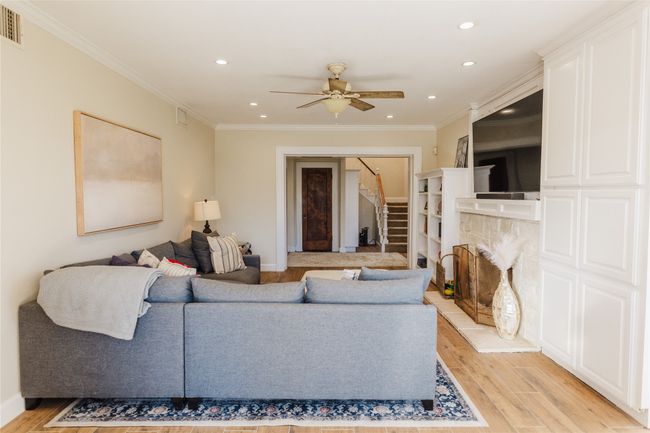 Living room featuring light wood-type flooring, ceiling fan, ornamental molding, and a fireplace | Image 13
