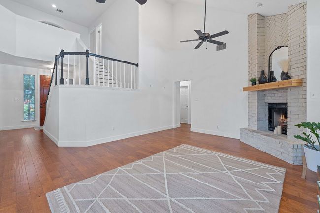 Unfurnished living room featuring ceiling fan, a high ceiling, hardwood / wood-style floors, a fireplace, and stairs | Image 16