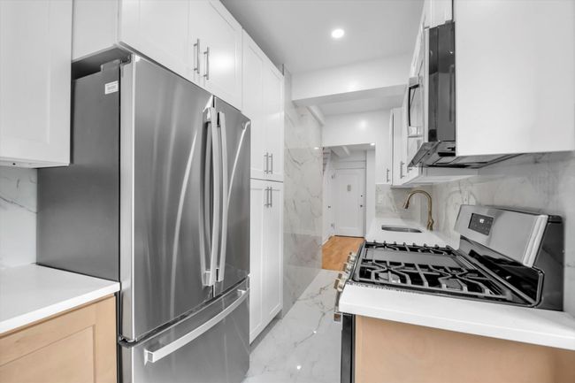 Kitchen featuring freestanding refrigerator, light marble finish floors, white cabinets, light countertops, and recessed lighting | Image 6