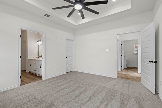 Unfurnished bedroom with light colored carpet, ensuite bath, ornamental molding, ceiling fan, and a raised ceiling | Image 32