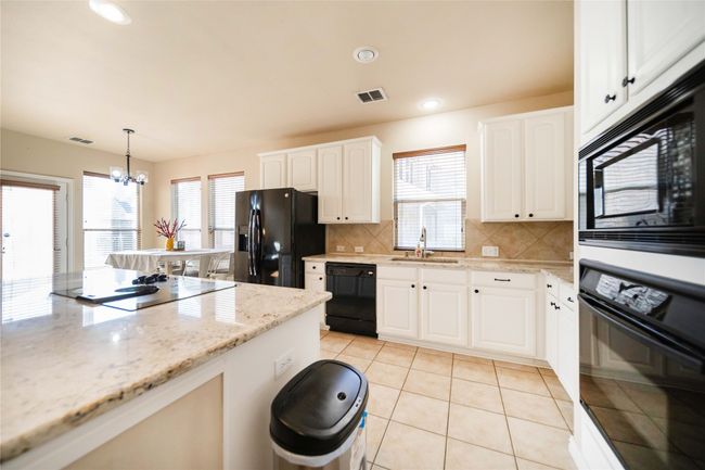 Kitchen with black appliances, a chandelier, decorative backsplash, hanging light fixtures, and white cabinets | Image 9
