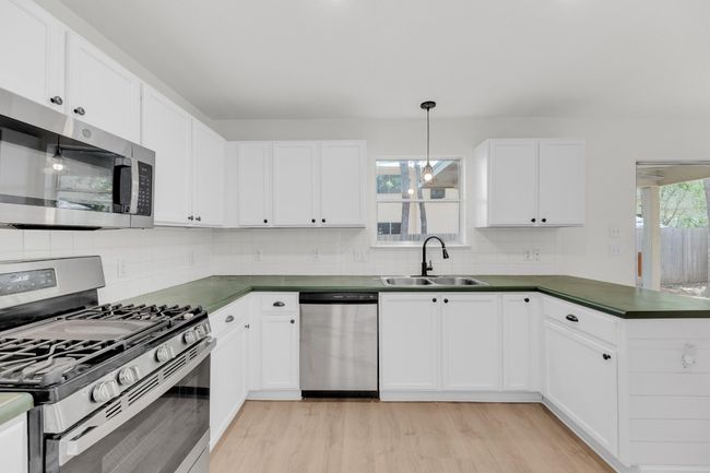 Kitchen featuring stainless steel appliances, a sink, dark countertops, backsplash, and light wood-style floors | Image 12