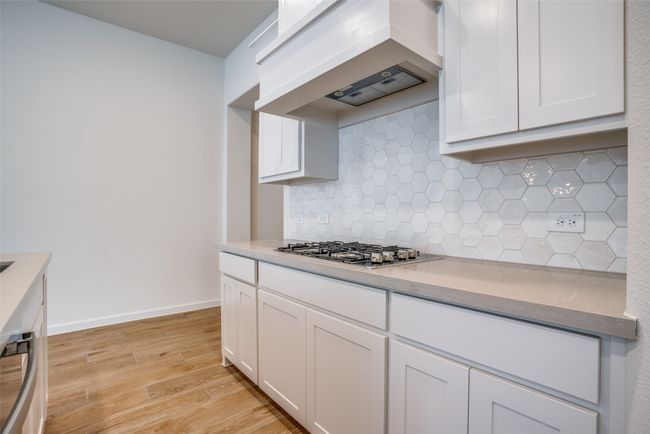 Kitchen featuring custom range hood, light wood-type flooring, white cabinetry, and tasteful backsplash | Image 12