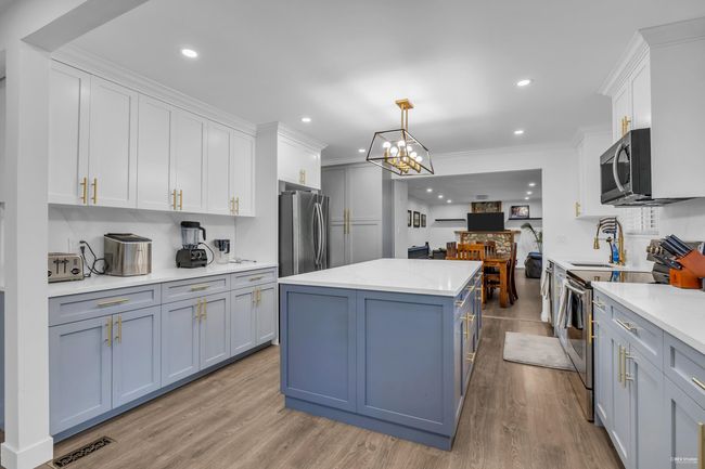 Kitchen featuring stainless steel appliances, a kitchen island, light countertops, white cabinets, and light wood-style flooring | Image 11