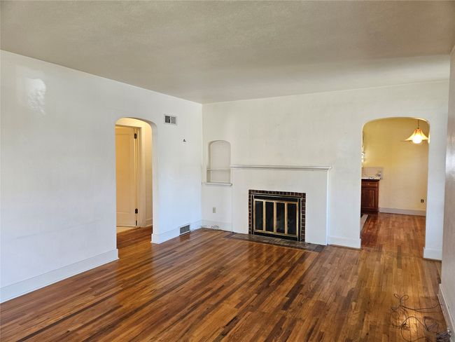 Unfurnished living room featuring visible vents, arched walkways, wood finished floors, and a brick fireplace | Image 8