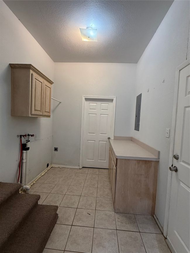 Washroom with cabinet space, a textured ceiling, light tile patterned floors, electric dryer hookup, and hookup for a washing machine. Two additional storage areas | Image 11