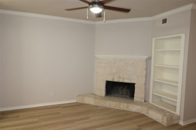 Unfurnished living room featuring wood finished floors, ceiling fan, ornamental molding, a stone fireplace, and baseboards | Image 4