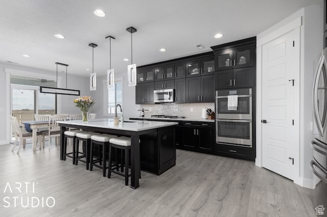 Kitchen featuring a breakfast bar, a sink, light countertops, appliances with stainless steel finishes, and dark cabinets | Image 9