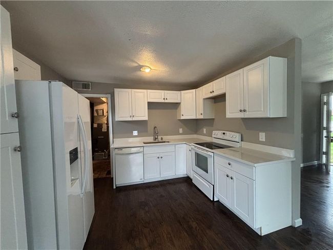 Kitchen with a sink, visible vents, white appliances, a textured ceiling, and dark wood finished floors | Image 10