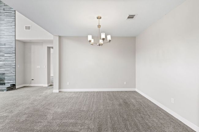 Carpeted empty room featuring a notable chandelier, baseboards, and visible vents | Image 10