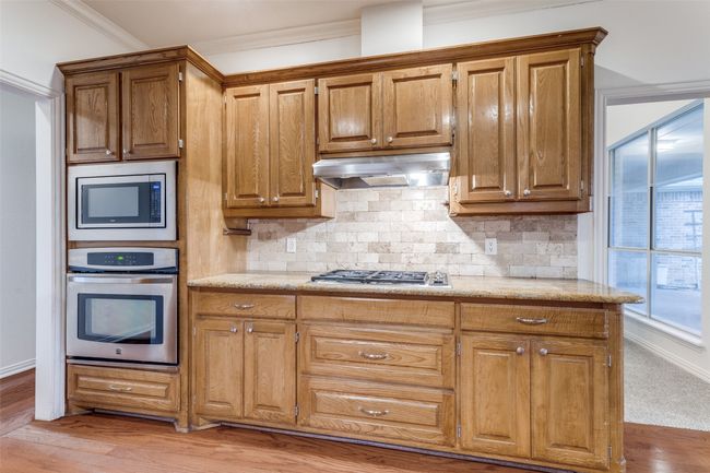 Kitchen with stainless steel appliances, under cabinet range hood, tasteful backsplash, ornamental molding, and light wood flooring | Image 12