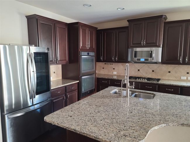 Kitchen featuring appliances with stainless steel finishes, light stone countertops, tasteful backsplash, dark brown cabinets, and recessed lighting | Image 8