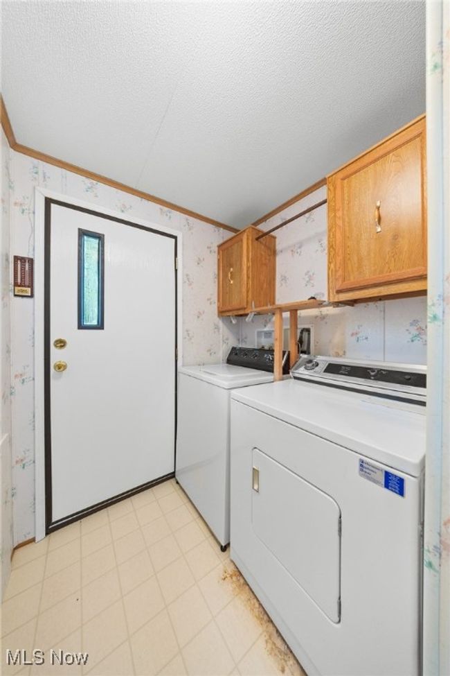 Laundry area featuring wallpapered walls, cabinet space, washing machine and dryer, ornamental molding, and a textured ceiling | Image 9