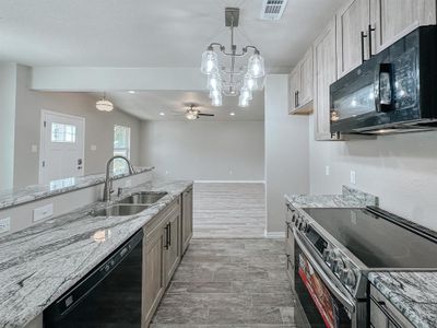 Kitchen with black appliances, sink, ceiling fan with notable chandelier, and light stone countertops | Image 1