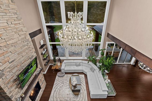 Interior space with an outdoor stone fireplace, a high ceiling, wood finished floors, and a notable chandelier | Image 19