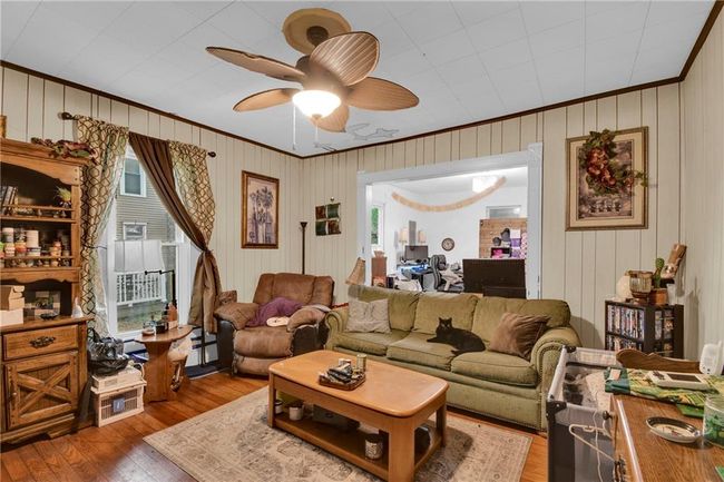 Living area with ornamental molding, hardwood / wood-style floors, ceiling fan, a baseboard heating unit, and wood walls | Image 4