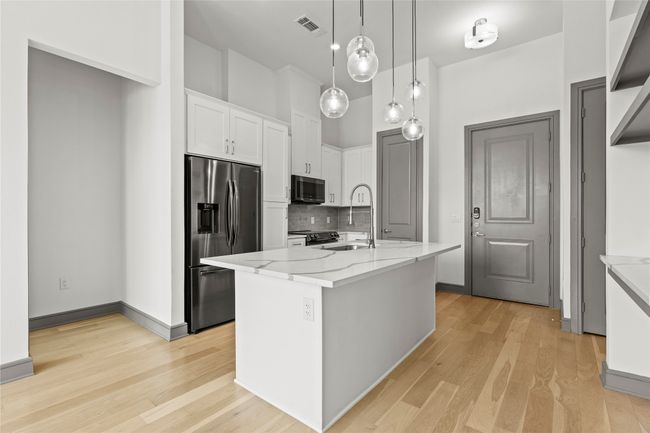 Kitchen with stainless steel fridge, a sink, light stone counters, light wood finished floors, and a high ceiling | Image 9
