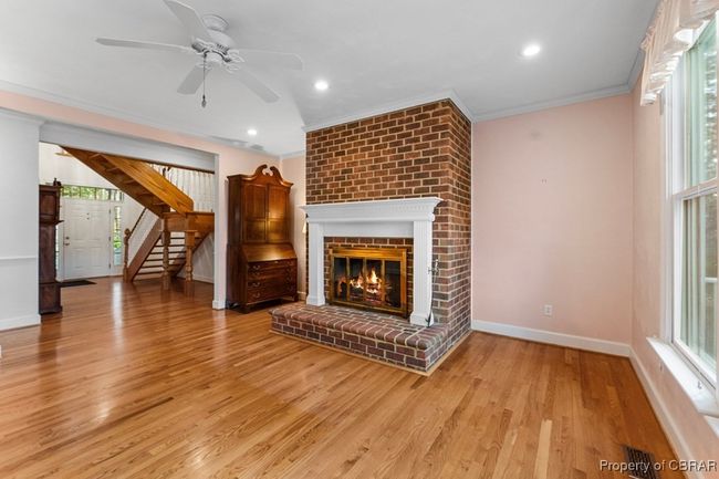 Unfurnished living room with crown molding, a ceiling fan, a fireplace, light wood-type flooring, and stairs | Image 17