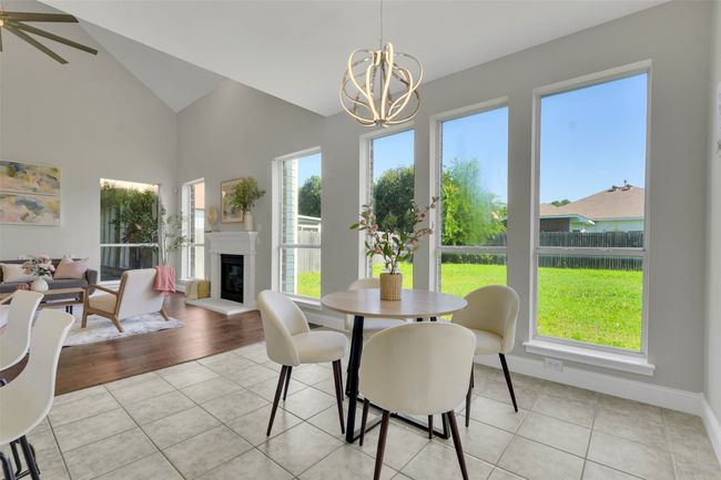 Dining room featuring a chandelier, light tile patterned flooring, a glass covered fireplace, and high vaulted ceiling | Image 12