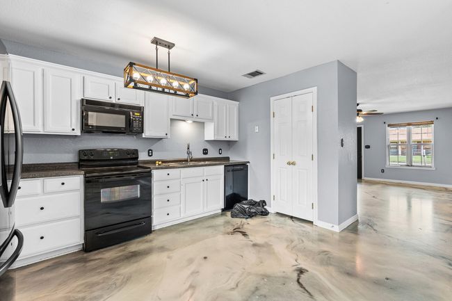 Kitchen with black appliances, white cabinets, finished concrete floors, dark countertops, and hanging light fixtures | Image 20