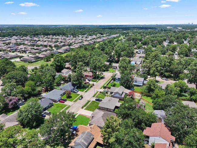 This aerial photo showcases a suburban neighborhood with tree-lined streets and a mix of single-family homes. The area appears peaceful and well-maintained, offering ample greenery and a sense of community. The homes have spacious yards, and the surrounding landscape provides a pleasant, natural setting. | Image 31
