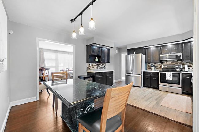 Kitchen with hanging light fixtures, backsplash, appliances with stainless steel finishes, dark wood-type flooring, and dark cabinetry | Image 13