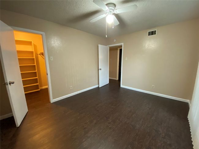 Unfurnished bedroom with visible vents, a spacious closet, dark wood-style floors, and baseboards | Image 17