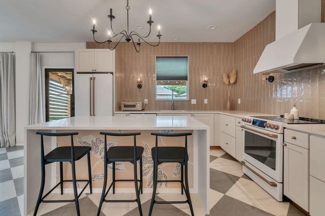 Kitchen featuring white appliances, wall chimney exhaust hood, light flooring, a sink, and white cabinets | Image 15