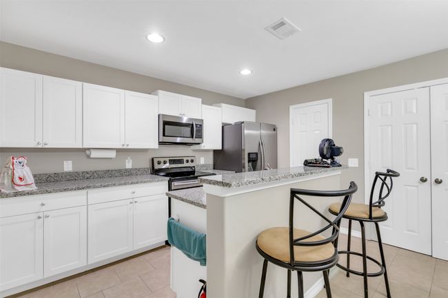 Kitchen featuring appliances with stainless steel finishes, light tile patterned floors, a breakfast bar, white cabinetry, and recessed lighting | Image 7