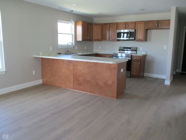 kitchen with light wood finished floors, brown cabinets, appliances with stainless steel finishes, a peninsula, and a sink | Image 5