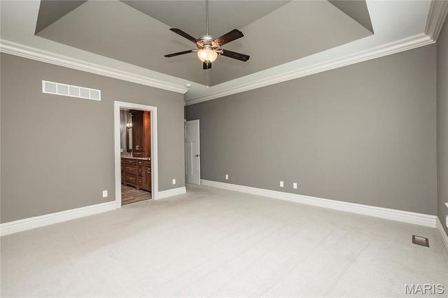 Primary first floor bedoom featuring ceiling fan, a tray ceiling, crown molding, and light carpet | Image 22