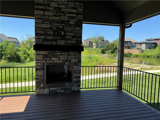 Wooden deck featuring an outdoor stone fireplace, a residential view, a water view, and a yard | Image 11