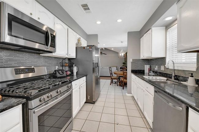 This kitchen features modern appliances, white cabinetry, and beautiful backsplash. The space is well-lit with recessed lighting and has a cozy dining area. | Image 9